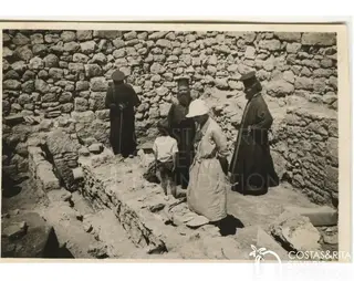 Three bearded clergymen, a woman in a white hat and a small boy stand among excavated stone walls