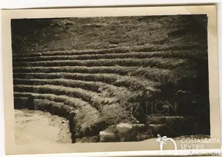 Curved rows of stepped seating running up a grassy slope, with stone blocks at the lower right