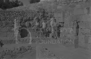 Three men stand beside draped marble statues against a stone wall at Salamis