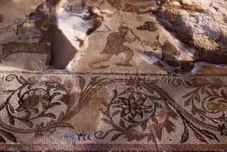 Floor mosaic with a small figure and scrolling foliage ornament, partly damaged