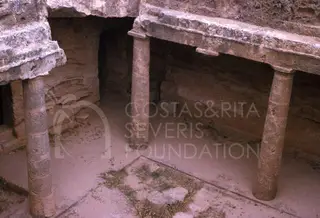 Rock-cut columns supporting a stone ledge in a tomb interior, with a dark opening behind