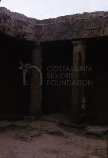 Rock-cut tomb front with two square pillars under a carved stone lintel, opening into dark chambers
