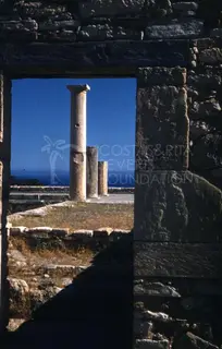 Three stone columns seen through a stone doorway, with blue sky and sea behind them