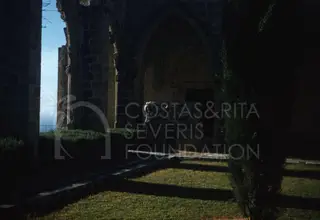 Carved stone sarcophagus in an arched passage of Bellapais Abbey, with grass and a cypress tree in front