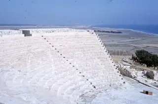 Curved white stone tiers of the theatre at Kourion, with flat land and sea beyond