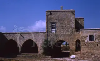 Stone building with arched openings and a square tower under a blue sky