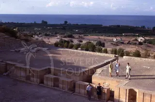 Five people among stone ruins at Soli, with the sea and houses beyond