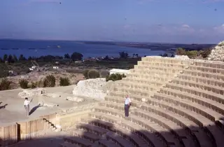 Stone theatre tiers at Soli descending toward a stage area, with the sea and ships in the distance