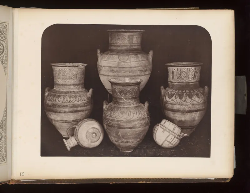 Five painted vessels with handles and banded decoration, with two smaller vessels lying in front, on a dark cloth.