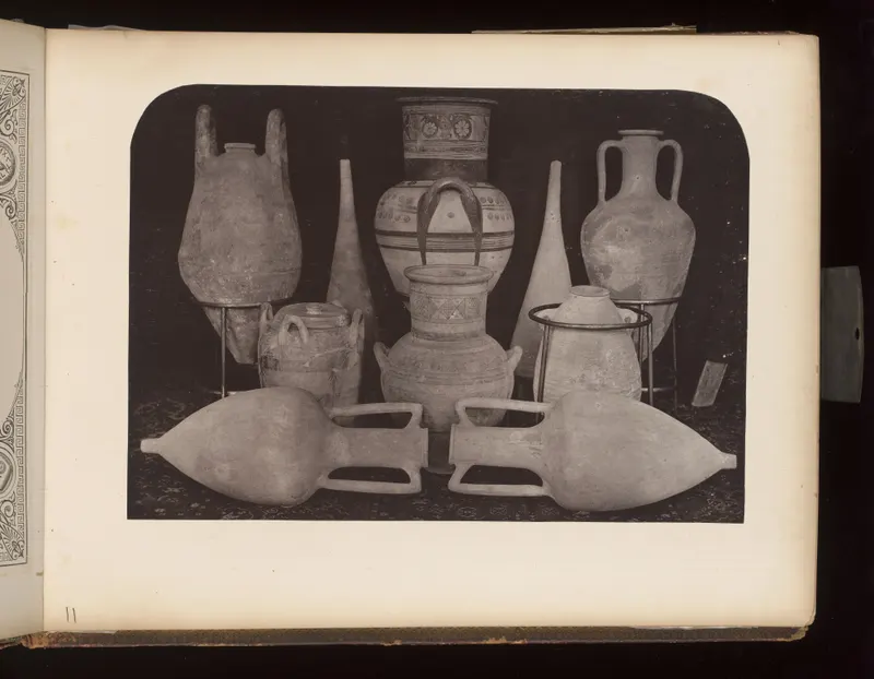 Group of terracotta vessels with handles, including large jars, amphorae and tall narrow flasks, arranged on a dark cloth.