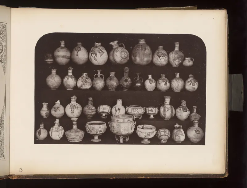 Rows of painted pottery jugs, juglets, bowls and a tripod vessel arranged on four shelves against a dark background.