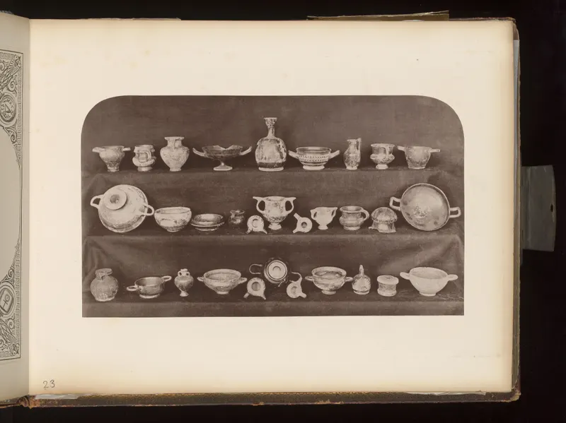 Many small pottery vessels arranged in three rows on dark shelves, including cups, bowls, jugs and lamps.