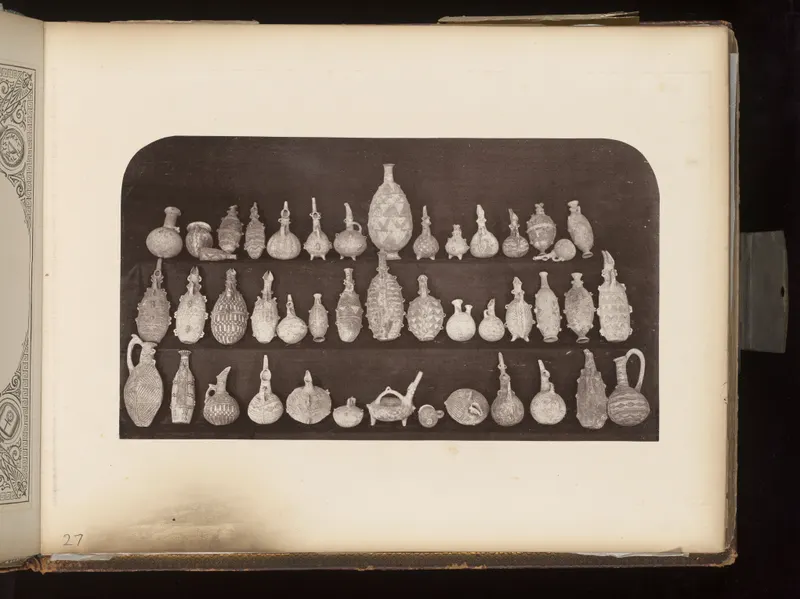 Rows of about forty small pottery jugs, juglets and bottles with painted bands and handles, set on a dark board