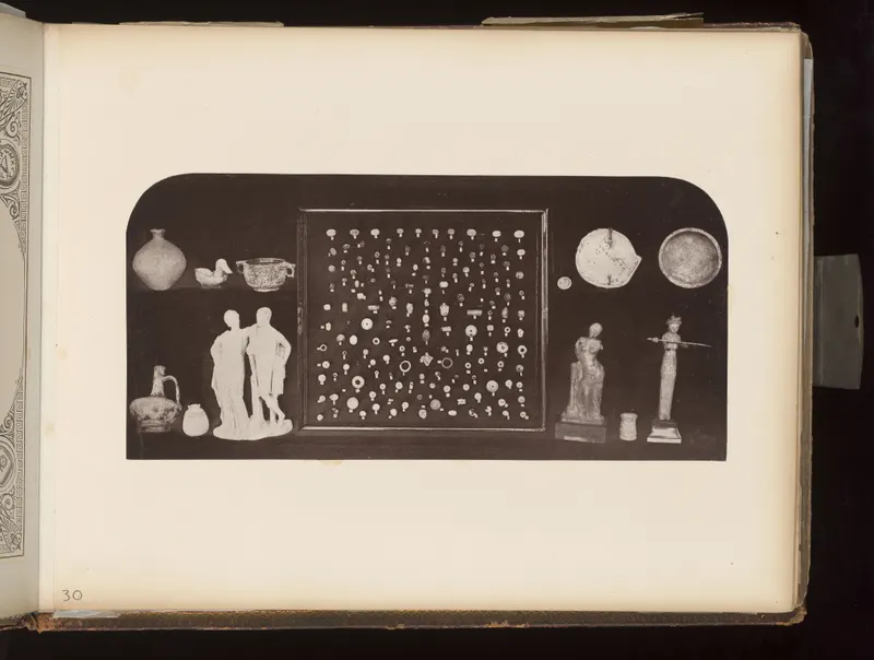 Dark board holding a jar, a duck-shaped vessel, figurines, a framed tray of small rings and beads, and dishes