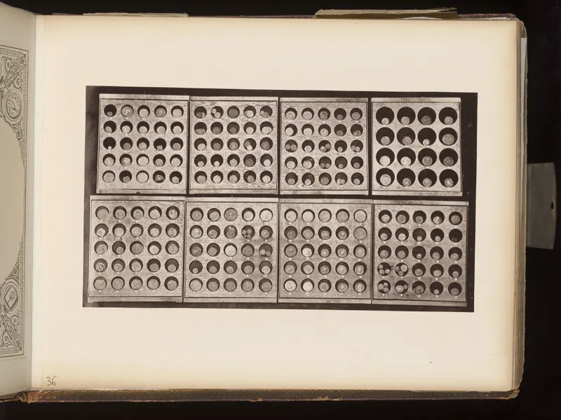 Eight wooden trays of small round coins in circular recesses, photographed from above, mounted on an album page.