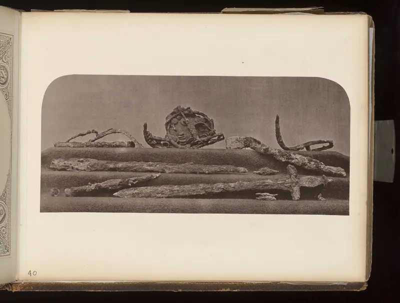 Corroded metal blades, a curved bit-like piece and a disc with a raised face, laid out on a cloth-covered shelf.