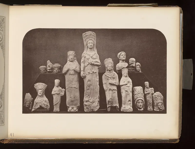 Pale statuettes and heads of figures with tall headdresses, arranged on dark boards against a dark background.
