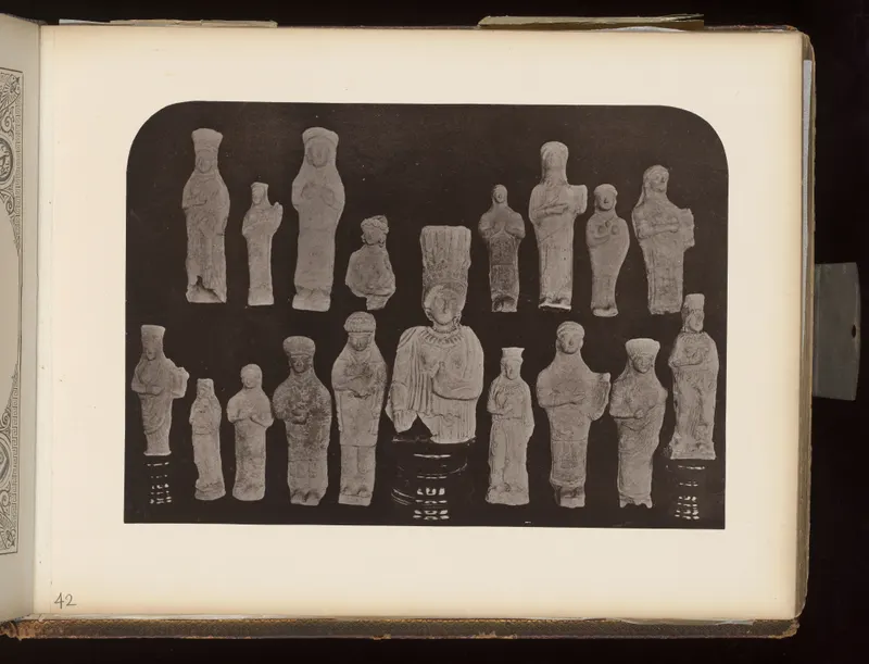 Two rows of about seventeen small pale figurines of standing figures against a dark background, on an album page.