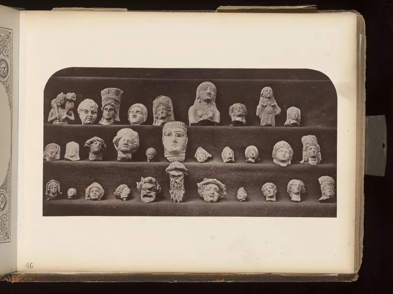 Rows of pale heads and small figures arranged on three dark velvet-covered shelves