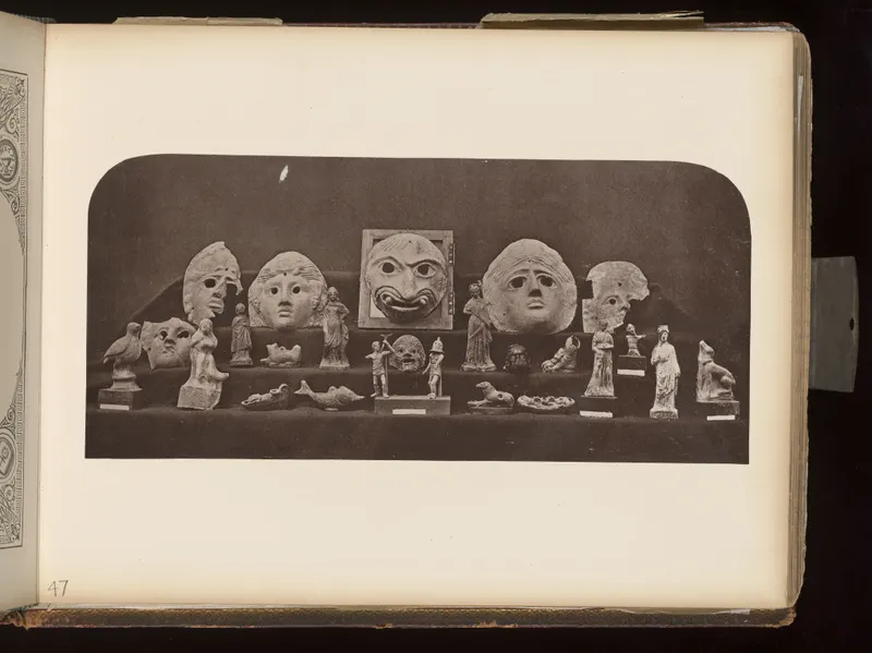 Masks, small figurines and animal figures arranged in rows on dark cloth shelves, mounted on an album page.
