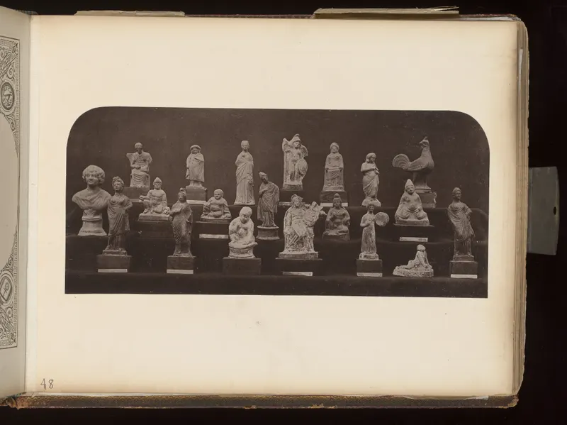 Rows of small figurines on stands, including a bust, draped standing figures and a cockerel, against a dark background
