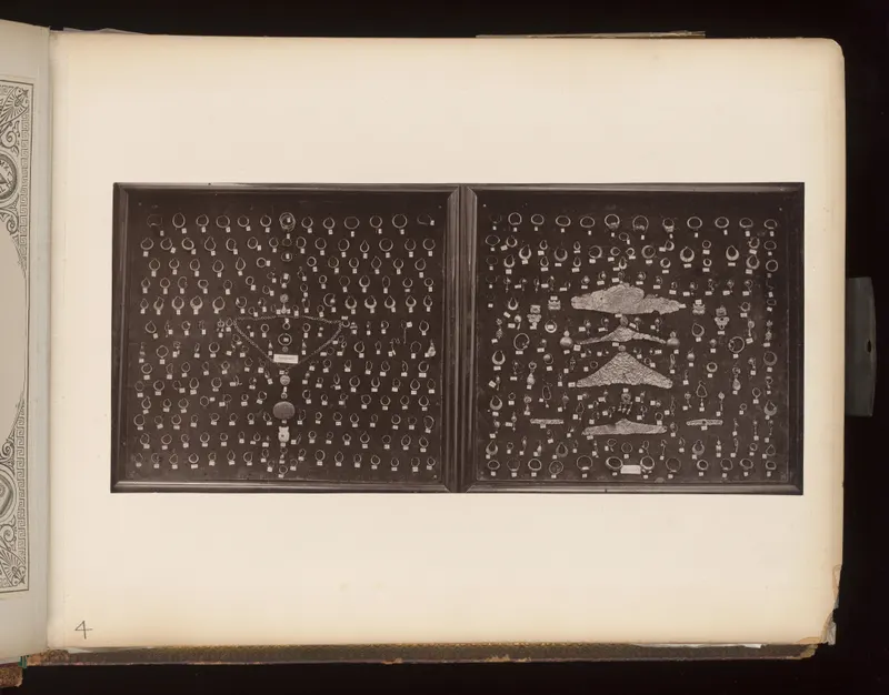 Two dark display trays holding rows of rings, earrings and beads, with a long chain and flat gold sheets.