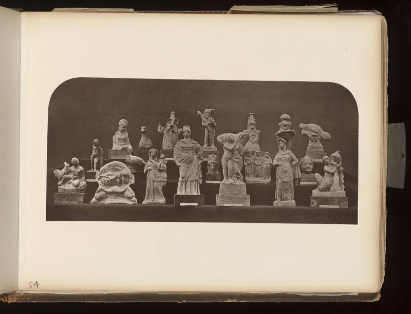 Many small terracotta figurines and heads arranged on stepped shelves against a dark background.
