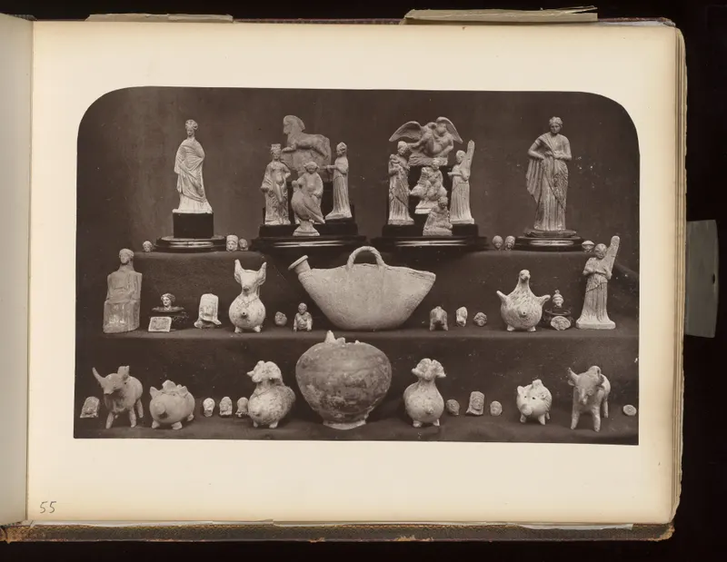 Pale figurines, animal figures and vessels arranged in tiers on dark cloth and black stands