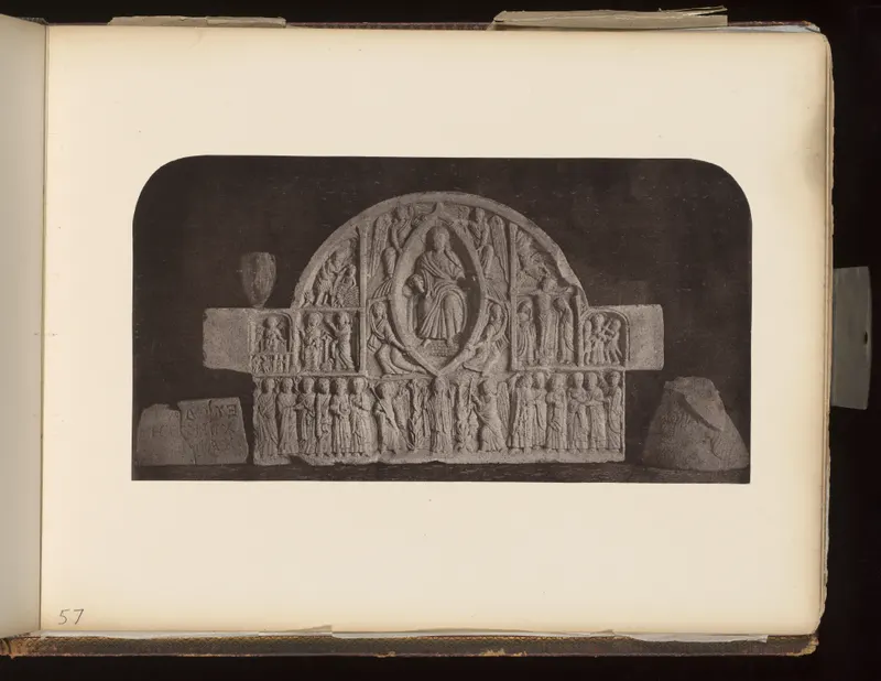 Arched carved stone relief panel with rows of small figures, flanked by two inscribed stone fragments on a dark background.