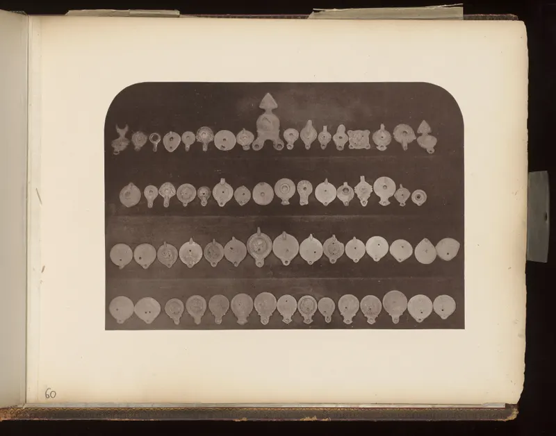 Four rows of small clay oil lamps with round discs and nozzles, laid out on a dark board.