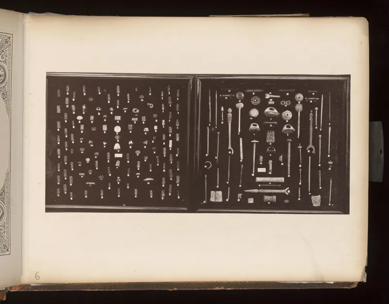 Two dark trays holding rows of small objects, pins, rods and rings, each with a small white tag