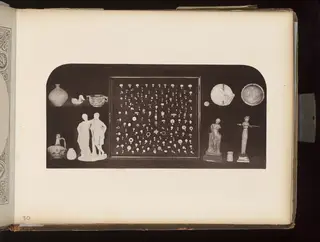 Dark board holding a jar, a duck-shaped vessel, figurines, a framed tray of small rings and beads, and dishes