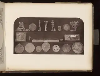 Rows of corroded metal disks, stands, a small figure and boxes laid out on a dark board