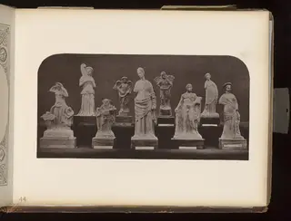 Eight small figurines of standing and seated figures on dark wooden bases, photographed against a dark background.