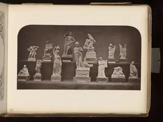 Terracotta figurines of human and animal figures standing and seated on small wooden bases, arranged on two tiers.