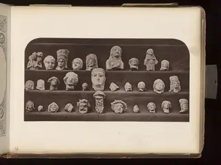 Rows of pale heads and small figures arranged on three dark velvet-covered shelves
