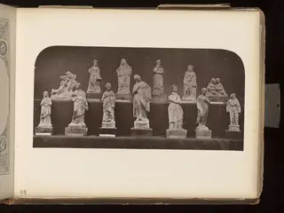Two rows of about a dozen small figurines on bases against a dark background, mostly standing draped figures
