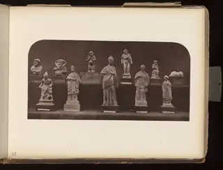 Row of about a dozen small figurines and one animal figure on wooden bases against a dark background