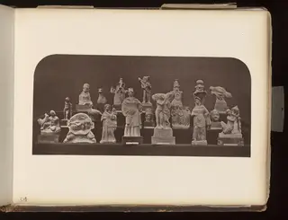 Many small terracotta figurines and heads arranged on stepped shelves against a dark background.