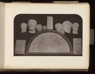 Carved stone heads above a half-round inscribed slab, with two rectangular slabs, against a dark background