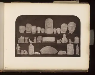 Stone heads in a top row, with small figures, reliefs and a fan-shaped slab in rows below, on a dark board.