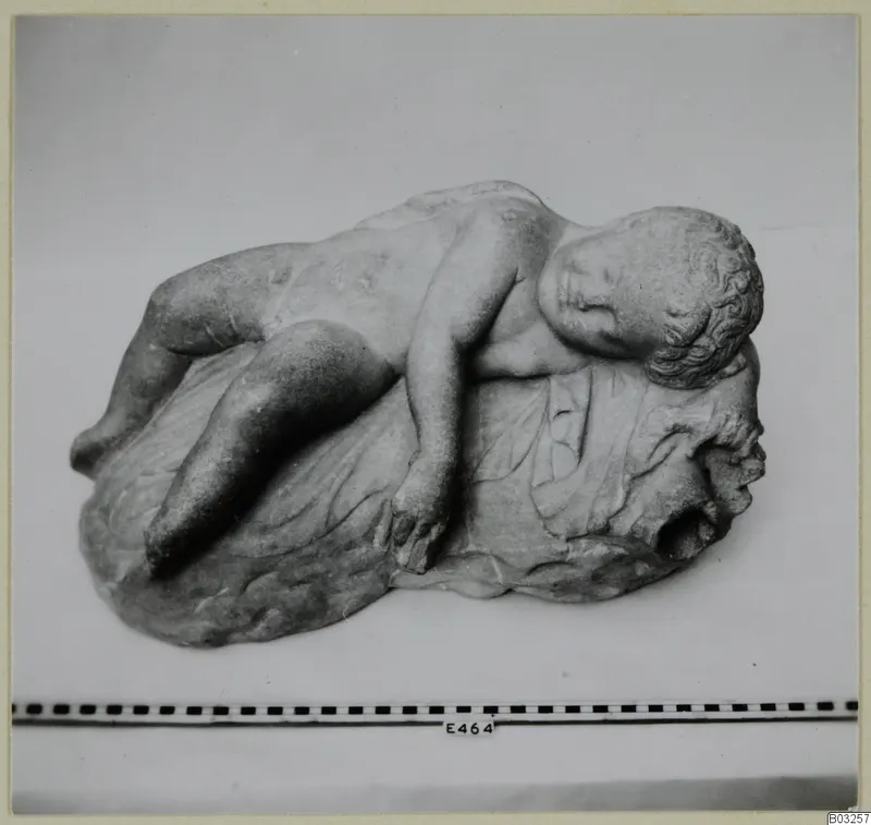 Marble sculpture of a sleeping child reclining on a draped base, head resting on one arm
