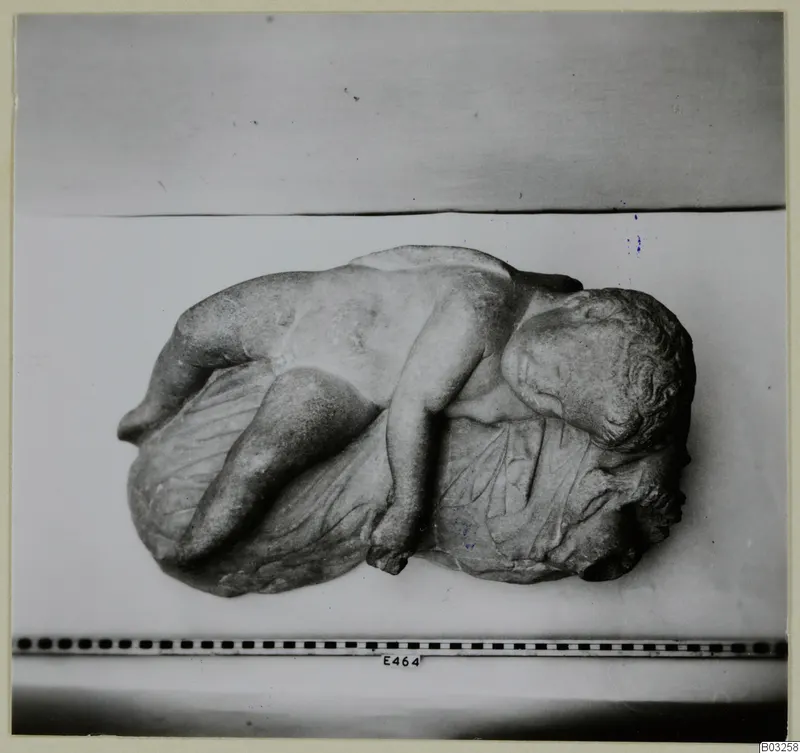 Marble sculpture of a reclining figure with curly hair, lying across a draped cloth
