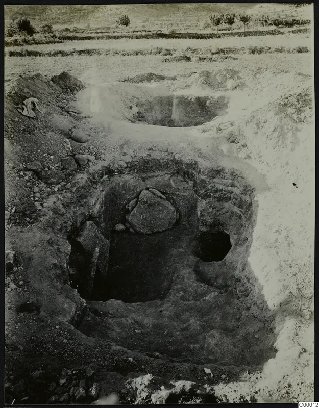 Tomb 315 at Lapithos during excavation, with a large stone lying inside the open tomb chamber and spoil heaps around it
