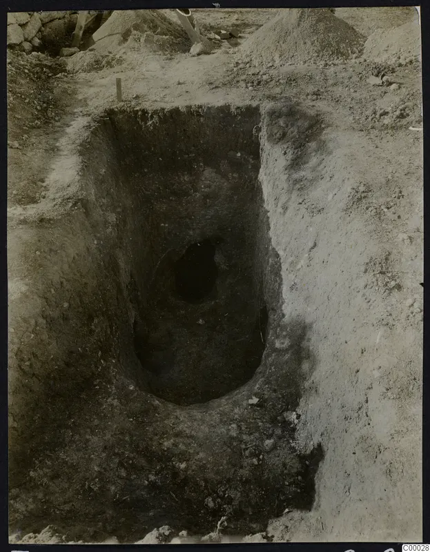 Tomb 302 at Lapithos during excavation, with a dark oval opening at the base of a deep rectangular cut in the soil