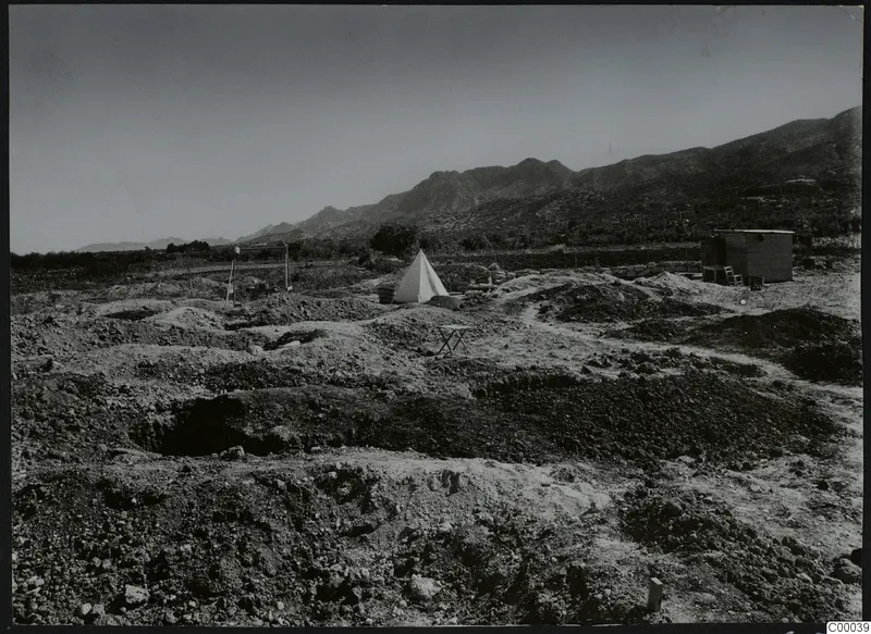 Excavation at Lapithos with mounds of earth and a white tent, with mountains behind.
