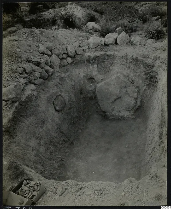 Tomb 320 at Vrysi tou Barba, Lapithos, during excavation, showing the cut chamber with a large stone and a box of stones