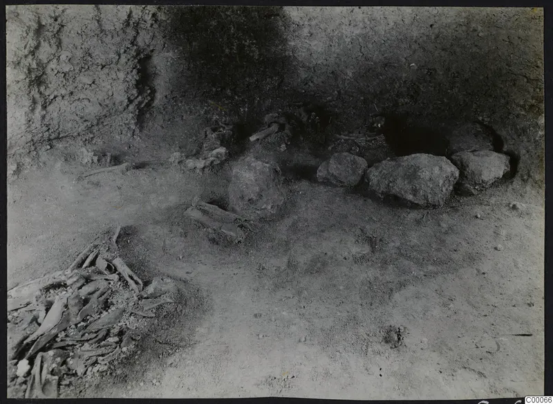 Tomb 303 a at Lapithos during excavation, with a jumbled skeleton in the lower left and large stones along the chamber wall.