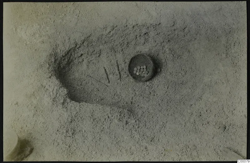 Tomb 322 at Lapithos during excavation, with a small vessel holding pale round objects in the sandy floor.