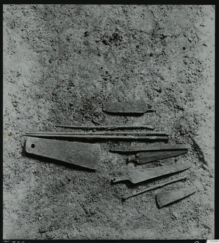 Corroded metal objects, including blades and pins, lying in soil during excavation of Tomb 322 at Lapithos